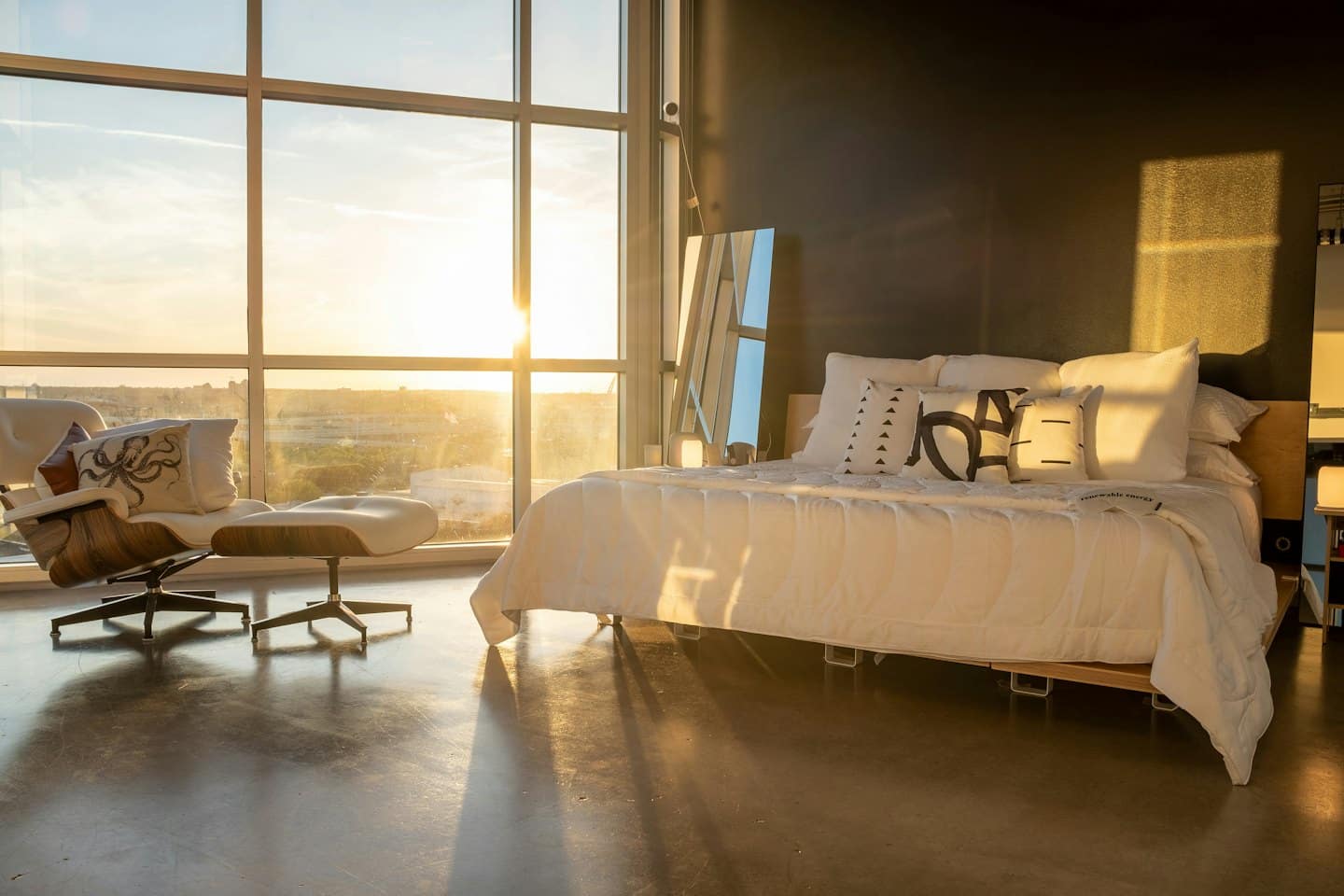 Moderna camera da letto con biancheria da letto bianca e poltrona alla luce dell'ora d'oro.