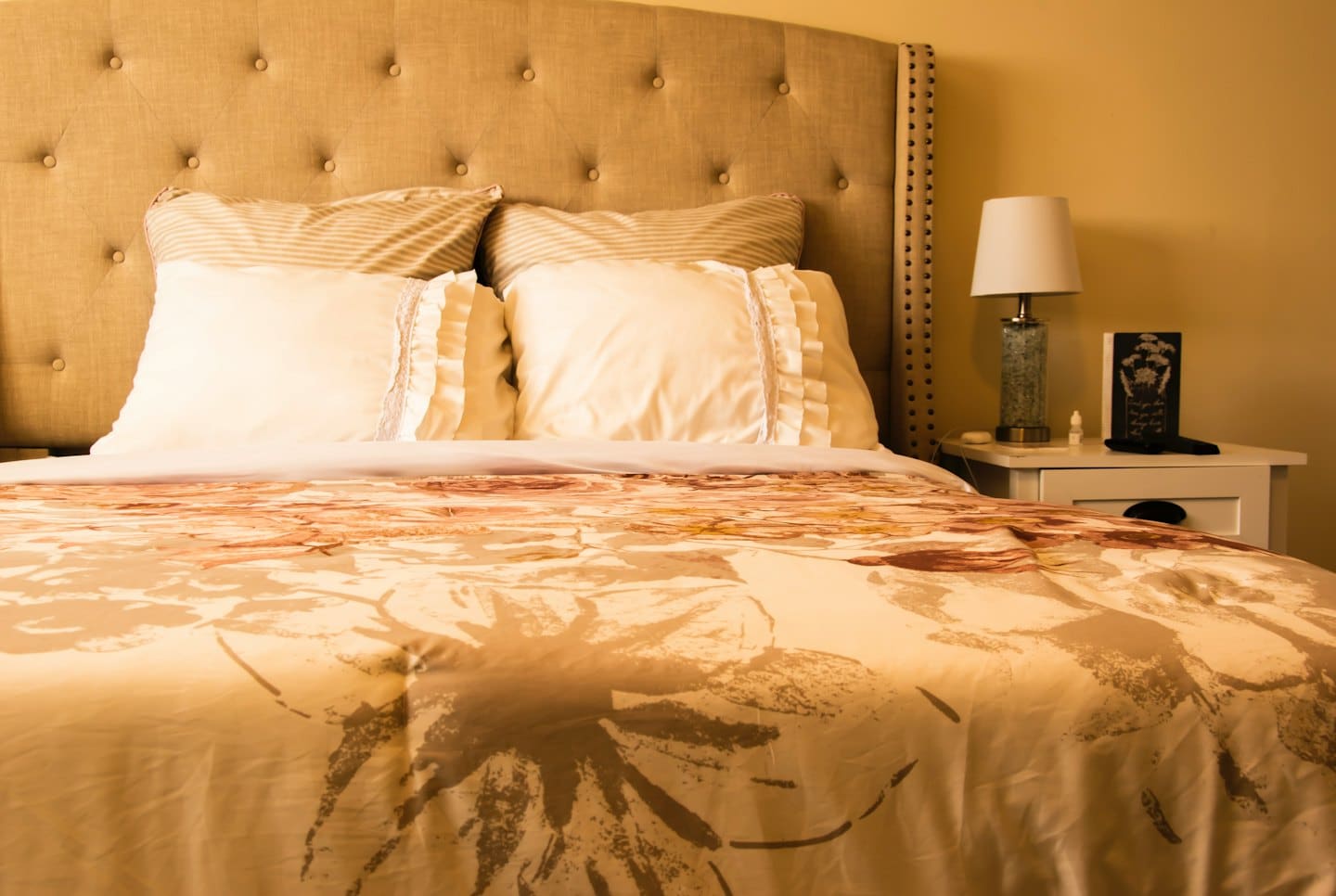 Un letto con testiera trapuntata, biancheria da letto floreale e un comodino.